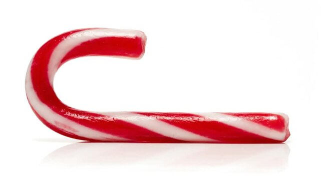 Single red and white striped candy cane resting on a reflective white surface, festive treat