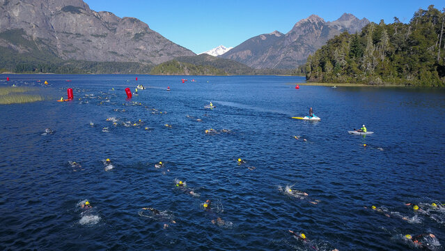 Aerial view of a swimming competition in a lake with swimmers in yellow caps, red buoys, and mountains in the background in San Carlos de Bariloche, Rio Negro Province, Argentina.