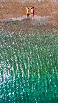 Couple in swimsuits lay on a sandy beach, top down view. Vertical