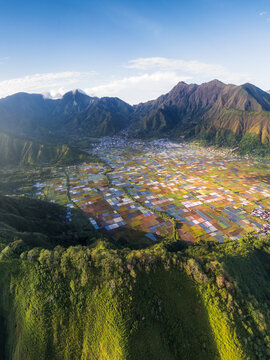 Aerial view of the lush Sembalun valley, featuring a patchwork of colorful agricultural fields nestled between dramatic mountain slopes. Sembalun, West Nusa Tenggara, Indonesia.