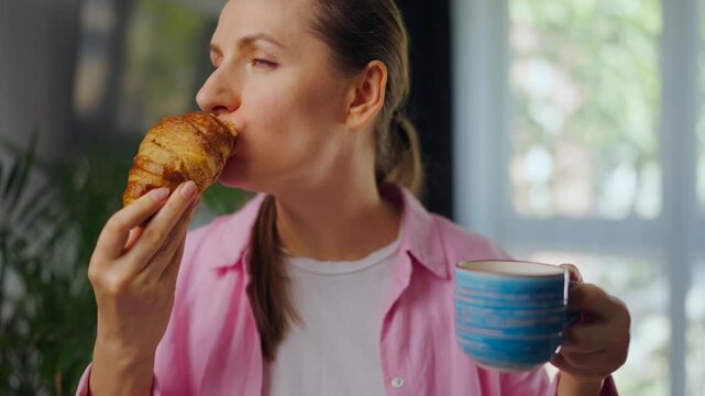 Woman enjoying a fresh croissant and coffee for breakfast.