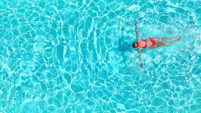 Top down view of a woman in pink swimsuit swimming on her back in the pool.