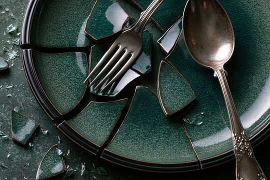 Shattered green ceramic plate with fork and spoon resting among broken shards.