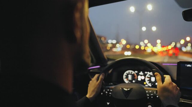Backseat view on man driving car through the streets of the evening city.