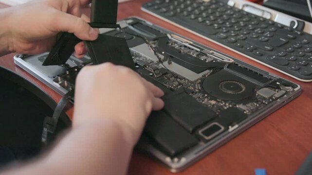 The master holds a disconnected battery with a cable over the opened laptop case for subsequent replacement