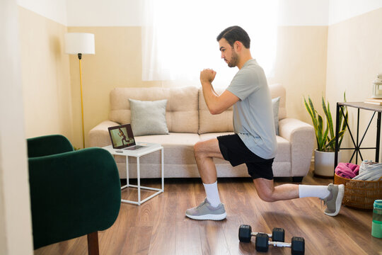 Man doing lunges during online fitness class at home, following virtual workout routine on laptop