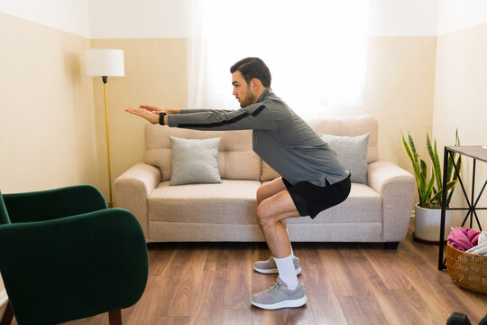 Profile view of a man doing squats in living room, maintaining active lifestyle with at-home fitness workout