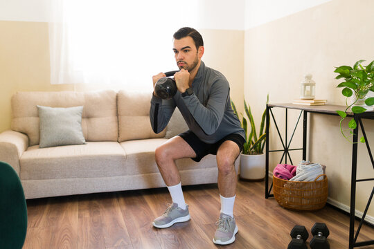 Focused man performing kettlebell squats at home, actively engaging in a wellness workout for strength and fitness