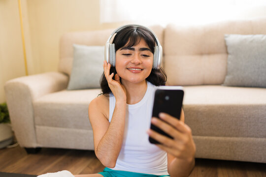 Young woman enjoying music on headphones while checking smartphone before home workout, preparing for fitness activity