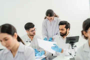Scientists in lab coats and glasses examining document together at desk with digital microscope, collaborative data review in bright lab. © Jestercine