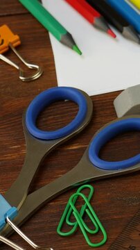 Scissors, colorful pencils, eraser, paper clips, and ruler scattered on wooden table. Office and school supplies provide organization. Stationery items enhance productivity