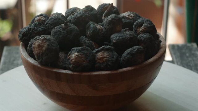A bowl of black maca rotates on a tray next to a window.