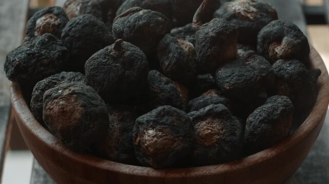 A bowl of black maca on a rustic wooden table.