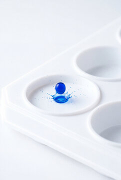 Blue reagent droplet captured mid splash on laboratory spot plate