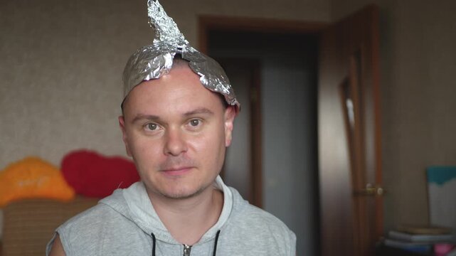 Man with foil headgear stands calm with distant gaze. Concept of conspiracy belief, shield from invisible waves, modern myth, psychological balance under media noise