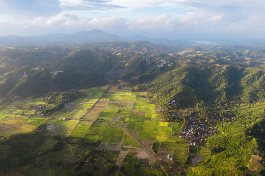 Aerial view of lush green rice fields and rolling hills surrounding the village of Selong Belanak in Praya Barat, West Nusa Tenggara, Indonesia.