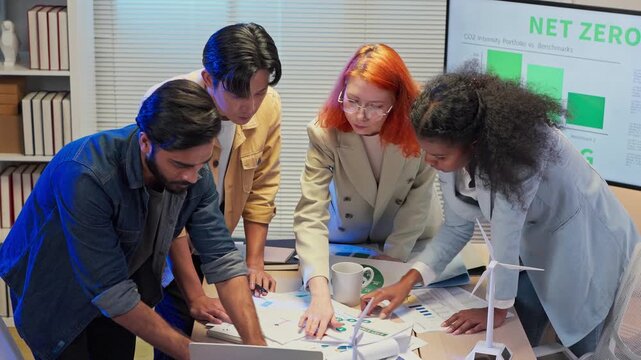 Diverse business team standing in office at night analyzing ESG strategy and clean energy solutions, multiracial analysts discussing sustainable growth plan, corporate consulting concept