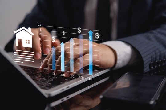 Real estate investment concept. Businessman hands typing on laptop with digital overlay of house icon, upward arrows, and dollar signs showing rising property values and market growth.