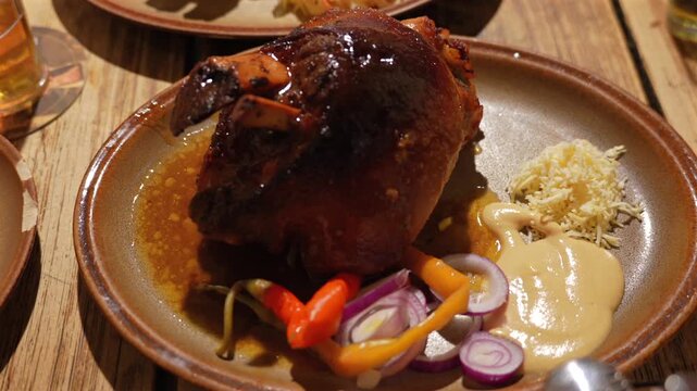 Czech roasted pork knuckle with mustard, horseradish and pickled peppers on a rustic plate.