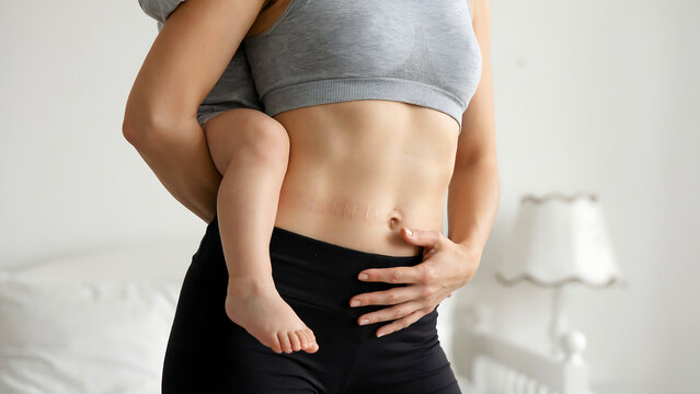 Fit mother holding her baby showing toned abs and healthy postpartum physique