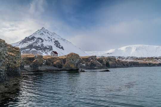 Snowy mountain and coastal house on rocky shoreline in Iceland