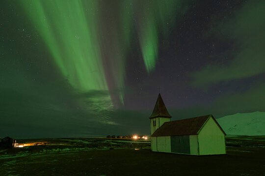 Aurora borealis over small church and snowy landscape in Iceland