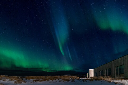Vertical northern lights over modern wooden house in snowy Iceland
