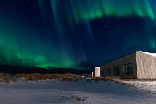 Northern lights over illuminated cabin and snowy dunes in Iceland