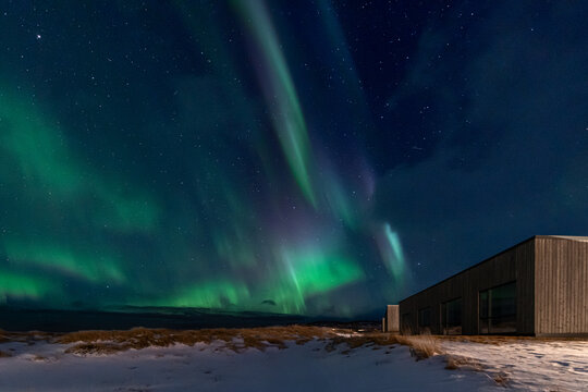 Northern lights over modern wooden cabin in snowy Icelandic landscape