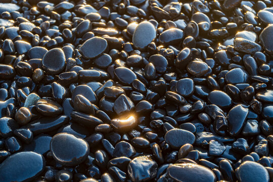 Wet black pebbles on a beach at sunset with golden sunlight reflections