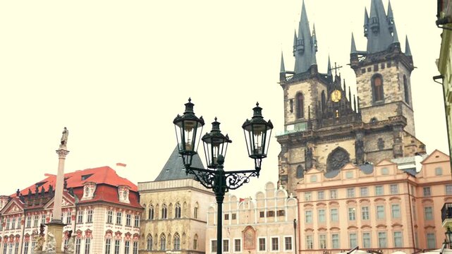 Gothic twin church towers rise above a historic town square framed by ornate street lamps and vibrant medieval facades.