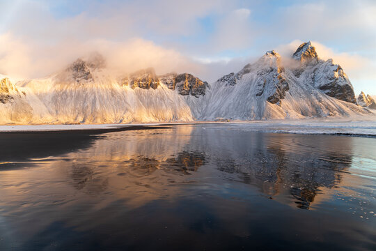 Iconic Vestrahorn mountain peaks with reflections in tidal pools on the Icelandic coast at sunrise.