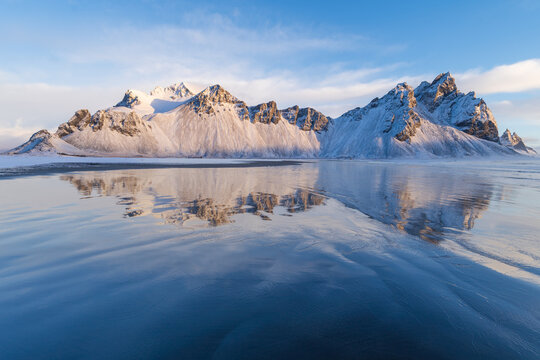Vestrahorn mountain reflected on wet black sand beach in winter, Iceland