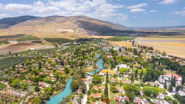 Aerial view of the kibbutz Nir David with its turquoise river flowing through lush greenery, surrounded by agricultural fields and mountains in Nir David, North District, Israel.