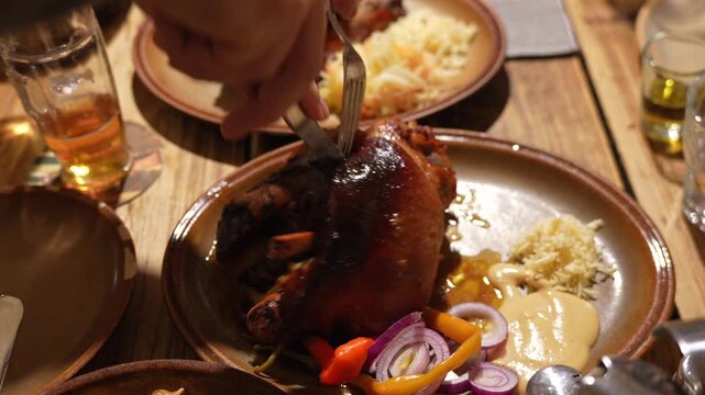 Czech pork knuckle carved at a rustic table with mustard, pickled peppers and onions in warm lighting.