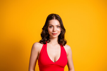 Obraz premium Young woman in a red halter dress smiling confidently against a vibrant yellow background, portrait of beauty, fashion and positive lifestyle