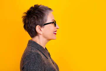 Smiling mature woman with short gray hair and glasses in profile against a bright yellow background, stylish portrait conveying confidence, joy and modern elegance © deagreez