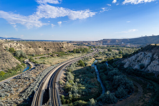 Aerial view of railroad tracks running through a desert landscape, the Jordan River, shrubs, and arid hills in Bluffdale, Utah, United States.