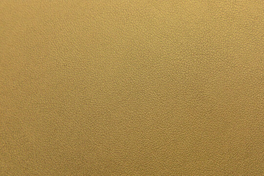 Gold leather texture background shows soft surface under bright light with fine details providing an abstract view of a warm color