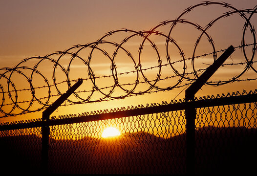Barbed wire on fence at sunset.