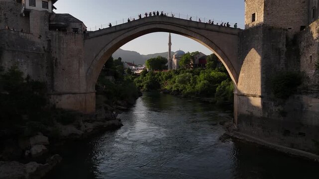 Drone flying under Stari Most bridge framing Koski Mehmed Pasha Mosque, Mostar Bosnia 4K