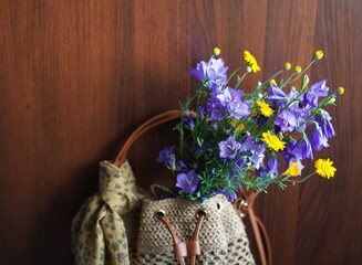 Close-up of a wicker straw summer bag with a blue bouquet of foxglove bells and yellow daisies and a tied cotton muslin orange scarf on a handle on a wooden background © Irina