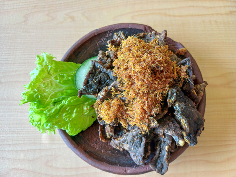 Fried beef lung or paru goreng served with spiced coconut flakes, cucumber slice, and lettuce on clay plate. Indonesian traditional culinary food top view.