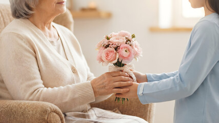 ソファに座る高齢女性へ感謝を込めて綺麗なピンクの花束をプレゼントする子供