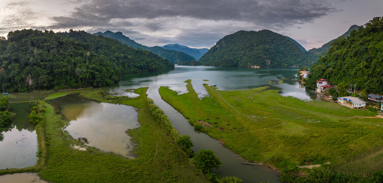 Aerial view of Ba Be Lake surrounded by lush green mountains, calm water, and small riverside houses in Ba Be, Thai Nguyen, Vietnam.