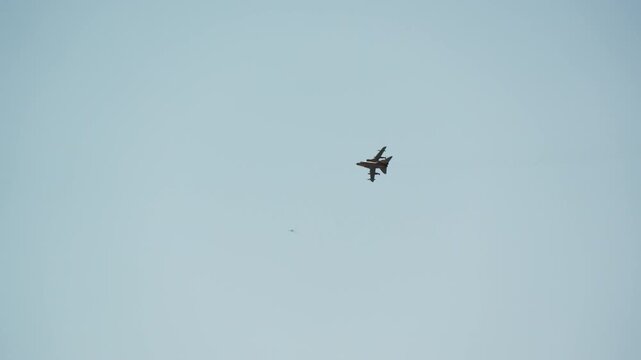 Military fighter jet flying high against a clear blue sky, fast combat aircraft banking during a display, slow motion shot of a single jet in open daytime sky
