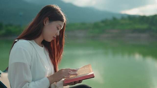 A woman reads a book at sunset. A girl reads the Bible in the open air. Female holding bible in hands and studying word of God at sunrise on top of mountain. Finding Truth in the Scriptures. 