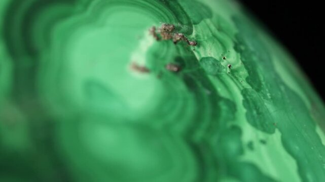 Malachite stone texture, extreme close up. Macro video of polished green stone with typical band patterns. Moving textures on black background