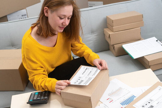 Woman putting shipping label on cardboard box working in her small business startup at home office