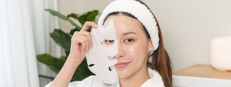 Beautiful Asian woman holding sheet mask off her face for skincare routine.